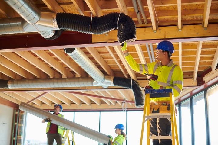 Workers install air ducts in a new building.