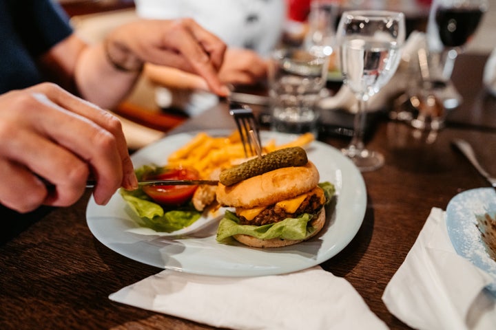 Close-up of a mid adult woman cutting cheeseburger in a restaurant.