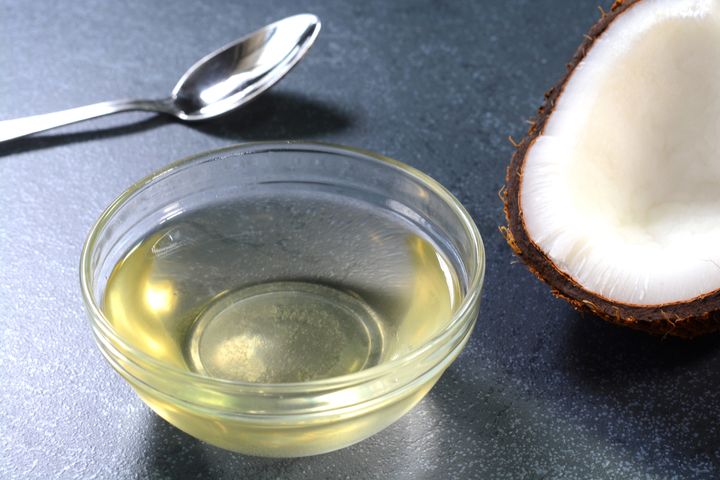 Coconut oil in a glass cup and split coconuts on the background.
