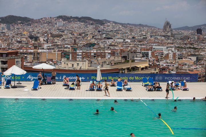 Tourists and residents enjoy the Municipal Pools of Montjuic where you can see the city of Barcelona in the background with the Basilica of the Sagrada Família.