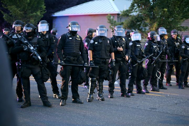 Portland police officers stand in a line holding their batons and guns on North Lombard Avenue during a protest at the police union building on on June 30, 2020.