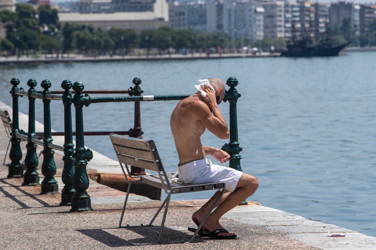 Άνδρας ξαποσταίνει σε ένα παγκάκι στην παραλία της Θεσσαλονίκης, σκουπίζοντας τον ιδρώτα του.
