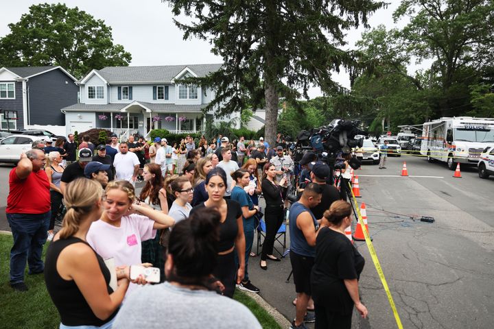 People watch as law enforcement officials investigate the home of a suspect arrested in the unsolved Gilgo Beach killings in Massapequa Park, New York, on Friday.