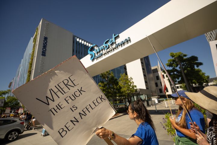 A demonstrator holds a sign reading "where the fuck is Ben Affleck" alongside striking WGA and SAG-AFTRA members.