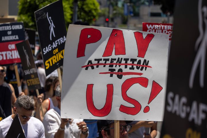 Outside Paramount Studios, a demonstrator holds a sign that reads, "Pay us!"