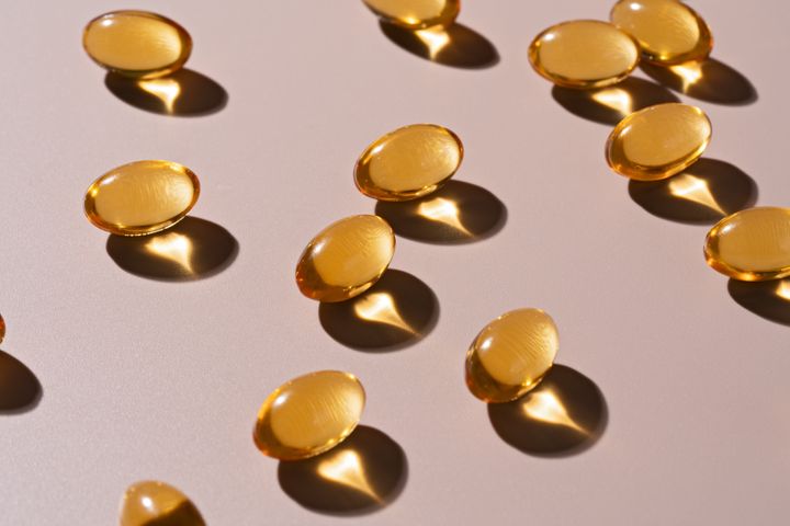 Gold Colored Soft Capsules of Fish Oil Flat Lay on Beige Background Directly Above View.