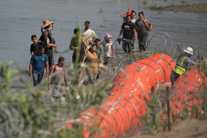 Migrants trying to enter the U.S. from Mexico approach the site where workers are assembling large buoys to be used as a barrier along the banks of the Rio Grande in Eagle Pass, Texas, on July 11. 