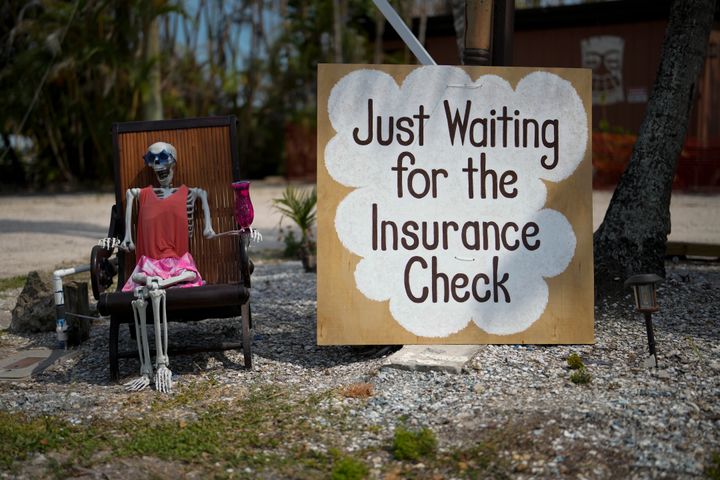A skeleton in sunglasses sits beside a sign reading "Just waiting for the insurance check," on Florida's Sanibel Island in May. The area was hit by Hurricane Ian in 2022.