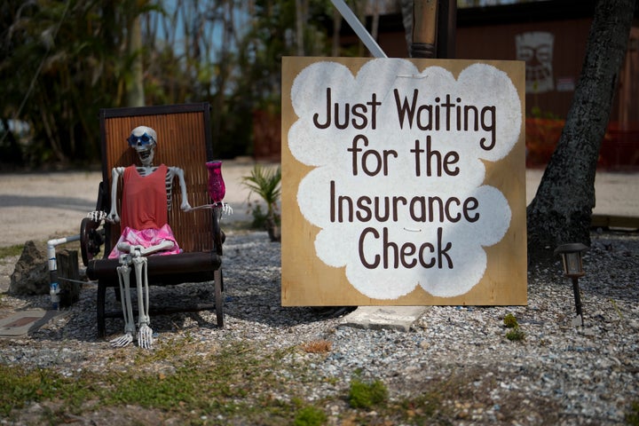 A skeleton in sunglasses sits beside a sign reading "Just waiting for the insurance check," on Florida's Sanibel Island in May. The area was hit by Hurricane Ian in 2022.