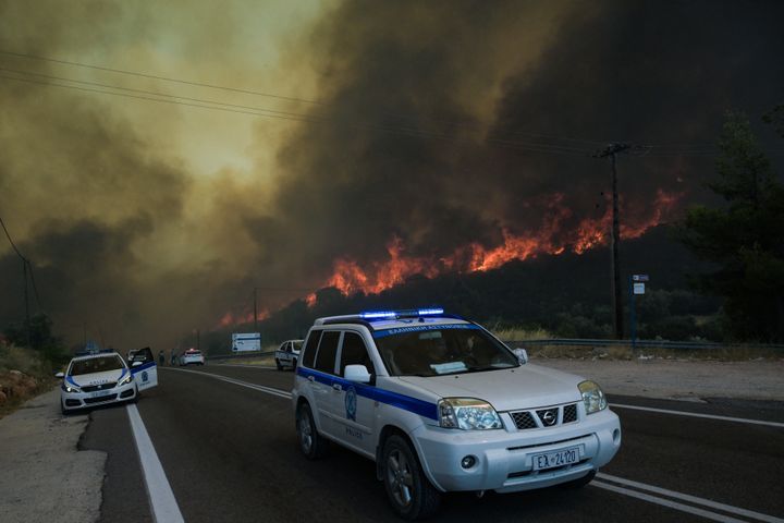 Petugas polisi mengevakuasi orang-orang dari daerah tersebut saat api membakar, di desa Agios Charalampos, dekat Athena, pada 18 Juli 2023.