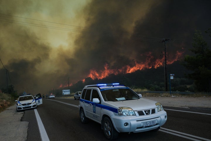 Police officers evacuate people from the area as a wildfire burns, in the village of Agios Charalampos, near Athens, on July 18, 2023.