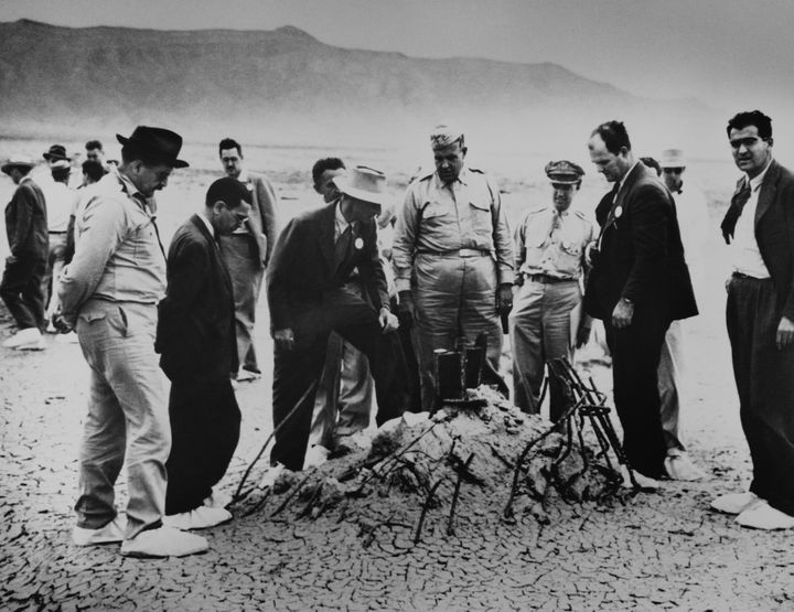 Oppenheimer e Gen. Leslie Groves ( centro ) examina os destroços retorcidos que restam de uma torre de 100 pés, um guincho e um barraco que segurava a primeira arma nuclear em Alamagordo, Novo México.