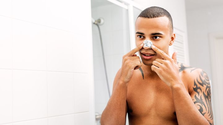 Young man applying nose patch in front of a mirror