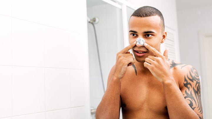 Young man applying nose patch in front of a mirror