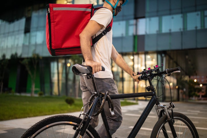 Delivery person with bicycle working late at night, he's wearing protective face mask