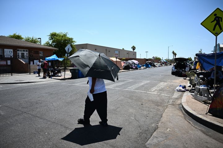 多くのホームレスの人たちが暮らす場所で、日傘を使い道路を渡る人（2023年7月18日）