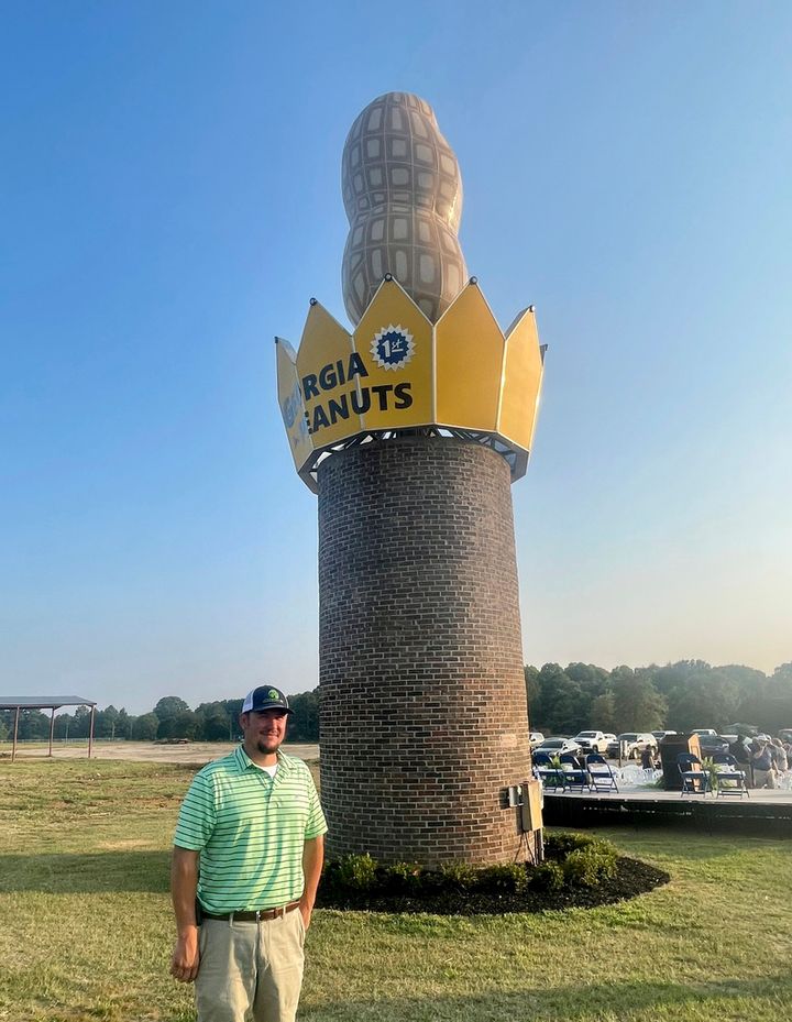 This photo provided by the Georgia Peanut Commission shows Cole Sercer of Sercer Machine & Fabrication, standing beside the Big Peanut that he and his employees designed and built near Interstate 75 in Ashburn, Ga., Thursday, July 20, 2023. The monument replaces a similar peanut that blew down during Hurricane Michael in October 2018. (Joy Crosby/Georgia Peanut Commission via AP)