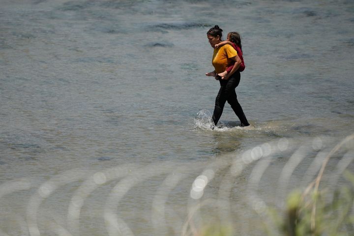 Migrants cross the Rio Grande from Mexico near the site where large buoys are being deployed to be used as a border barrier in Eagle Pass, Texas, on July 12, 2023. 
