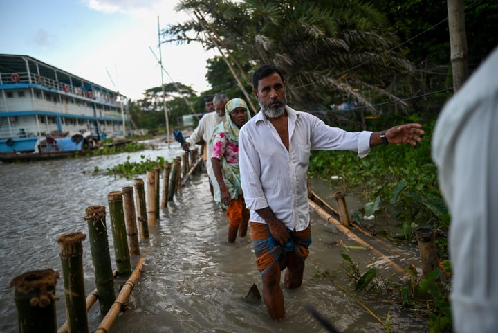 People walk through a flooded road due to rising tides at the bank of the Arial Khan River in Barishal, Bangladesh on July 15, 2023.