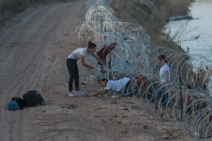A woman from Colombia helps her children crawl past concertina wire, deployed to deter migrants, after they crossed the Rio Grande river into Eagle Pass, Texas, on July 27.