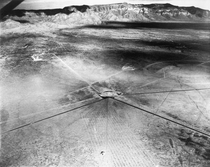 This aerial view of the atomic bomb testing site near Alamogordo, New Mexico, shows the shallow crater dug by the blast 300 feet around the tower from which the bomb hung. The sand in an area 2,400 feet around the tower was seared into jade green glasslike cinders. The area devastated by the bomb measures 4,800 feet in diameter, and the steel tower was entirely disintegrated.