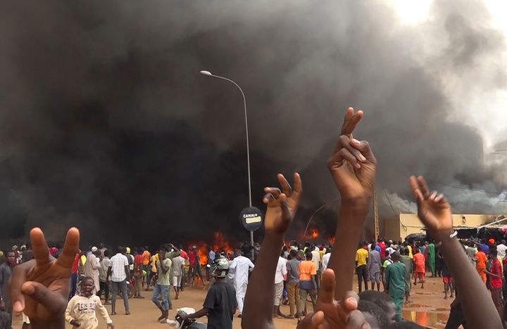 With the headquarters of the ruling party burning in the back, supporters of mutinous soldiers demonstrate in Niamey, Niger, on July 27, 2023.