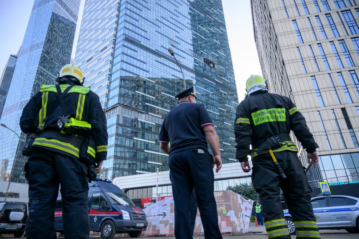 Firefighters and a police officer stand next to a damaged building in the "Moscow City" business district after a reported drone attack in Moscow, Russia, early on Aug. 1, 2023.