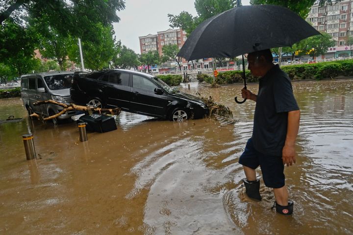 A man wades past a damaged car along a flooded street, after heavy rains in Mentougou district in Beijing on July 31, 2023.