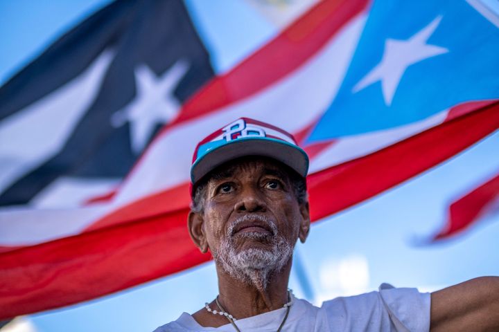 A man stands in front of Puerto Rican flags as he protests outside the headquarters of LUMA Energy, the company that took over the transmission and distribution of the island's electric authority, after a blackout hit the island two days earlier, in San Juan, Puerto Rico, on April 8, 2022.