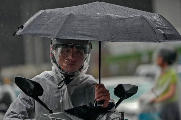 Ανδρας προστατεύεται με ομπρέλα πάνω σε μιηχανάκι, από τροπική καταιγίδα στο Πεκίνο, 1 Αυγούστου 2023.