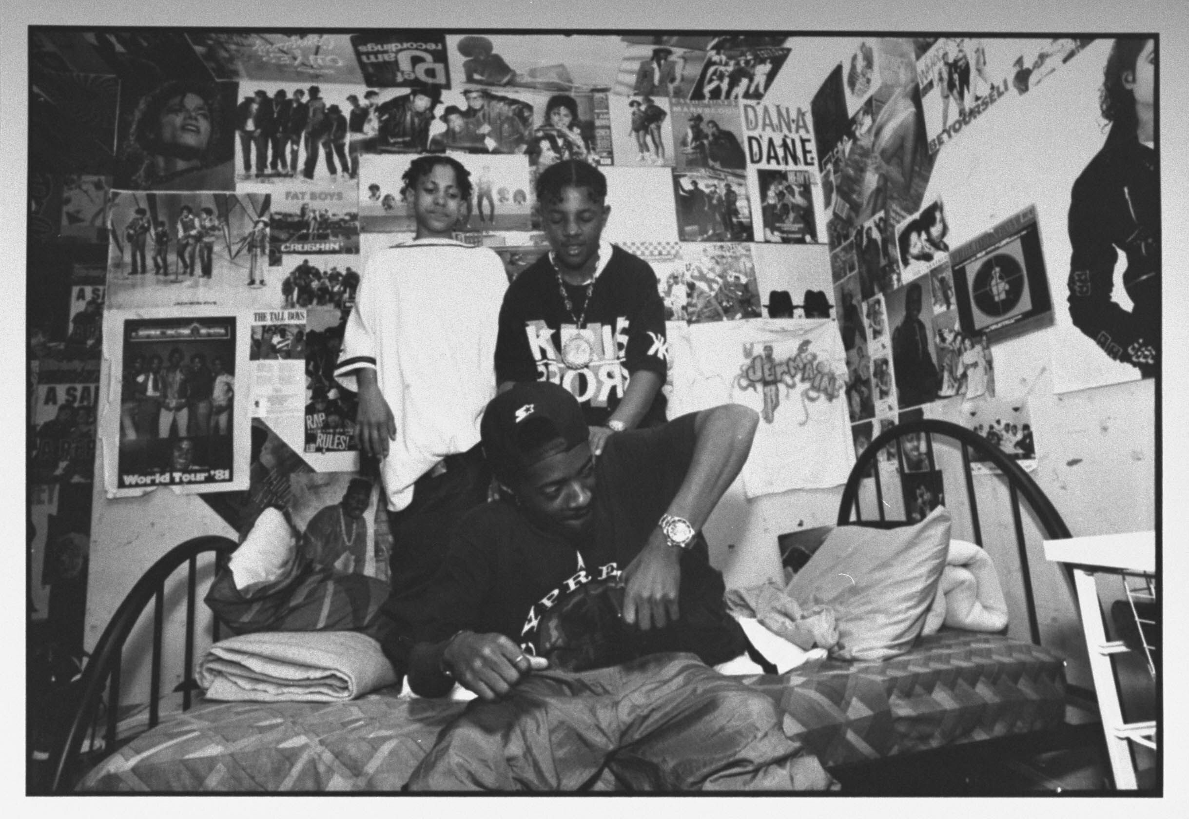 Kris Kross rap duo Daddy Mac (Chris Smith) and Mac Daddy (Chris Kelly) stand on a bed as they playfully rough up Dupri, their manager.