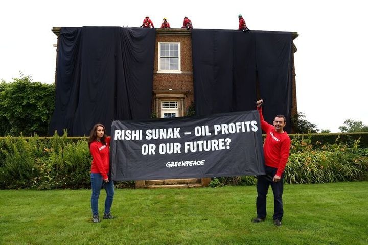 Ακτιβιστές της Greenpeace κρατούν πανό, ενώ άλλοι καλύπτουν το αρχοντικό του Βρετανού πρωθυπουργού Ρίσι Σούνακ, αξίας 2 εκατομμυρίων λιρών, με μαύρο ύφασμα σε ένδειξη διαμαρτυρίας για την υποστήριξή του σε μια σημαντική επέκταση των γεωτρήσεων πετρελαίου και φυσικού αερίου στη Βόρεια Θάλασσα εν μέσω ενός καλοκαιριού κλιμακούμενων κλιματικών επιπτώσεων, στο Γιόρκσαϊρ της Βρετανίας στις 3 Αυγούστου 2023.