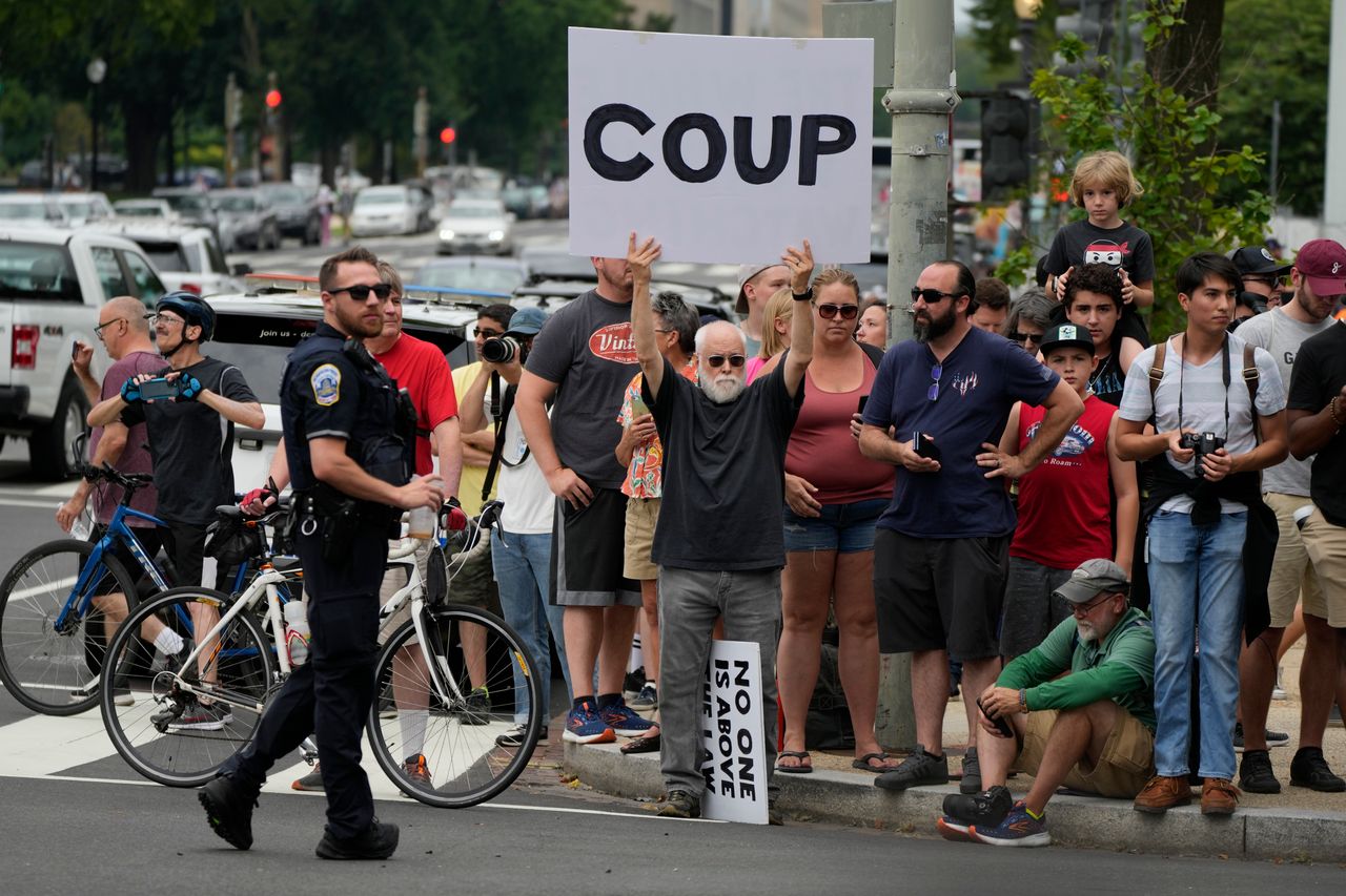 People gather, one with a sign that reads "COUP," before Trump arrives at the courthouse.