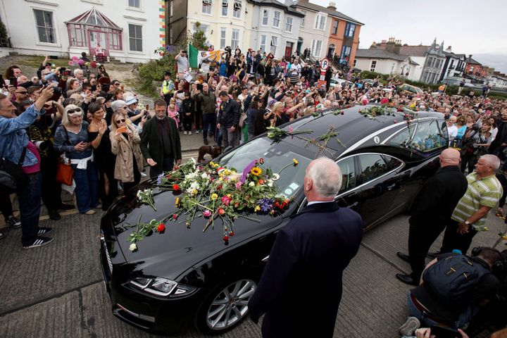 People lay flowers and tributes on the hearse during the funeral procession of late Irish singer Sinead O'Connor, outside the former home in Bray, eastern Ireland, ahead of her funeral on August 8, 2023. 