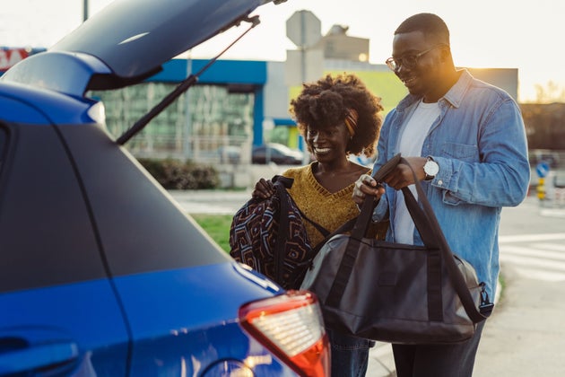 Smiling woman and man packing their travel bags into car trunk