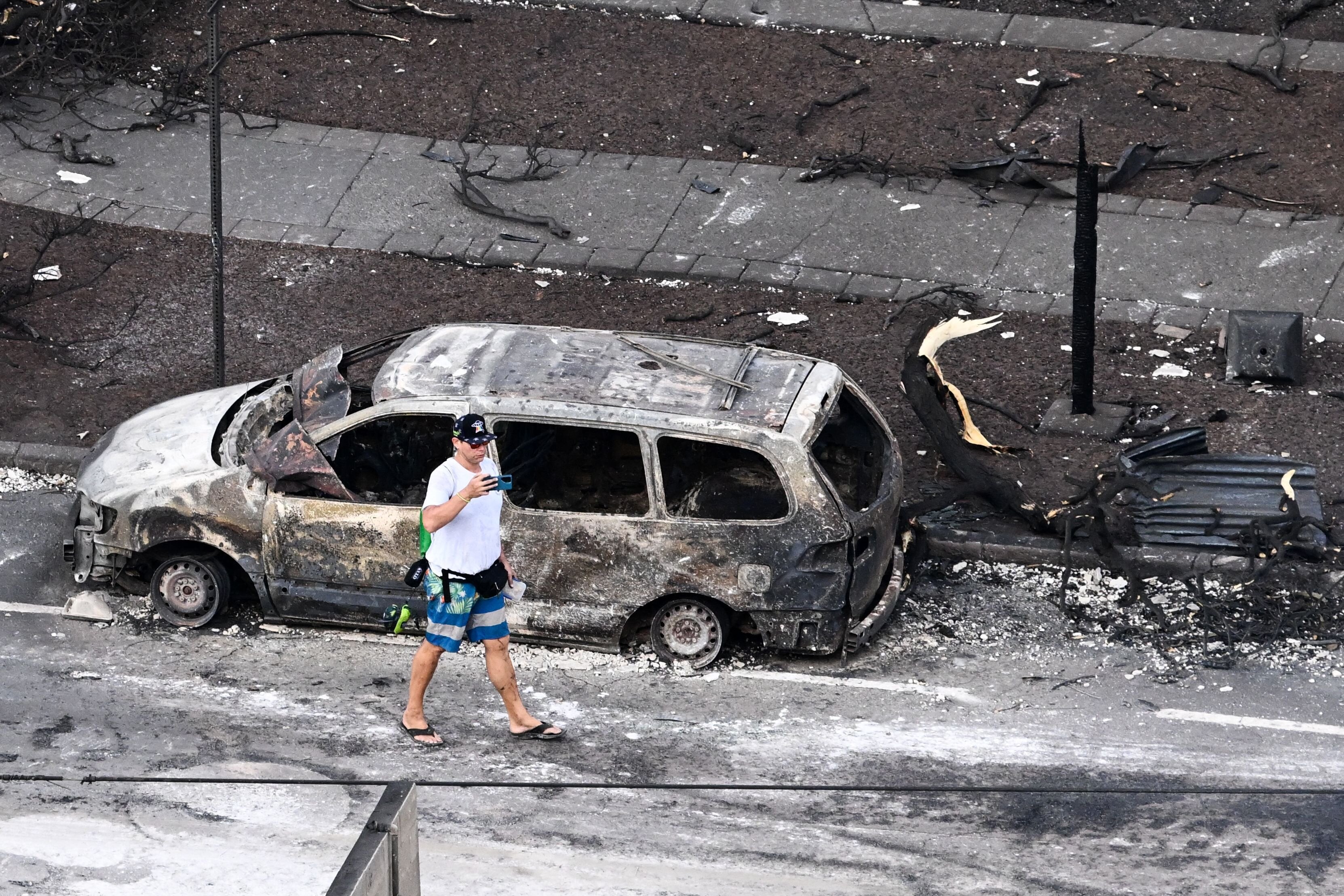 Person walking by a burned car in Lahaina