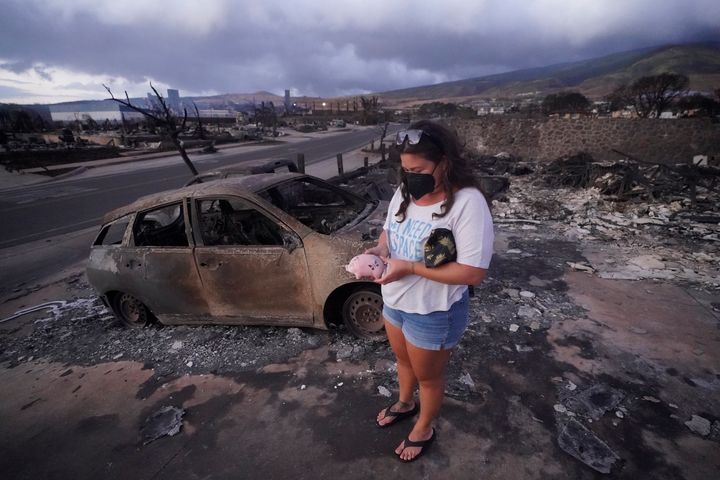 Summer Gerlingpicks up her piggy bank found in the rubble of her home following the wildfire Thursday, Aug. 10, 2023, in Lahaina, Hawaii. Hawaii emergency management records show no indication that warning sirens sounded before people ran for their lives from wildfires on Maui that wiped out a historic town.(AP Photo/Rick Bowmer)
