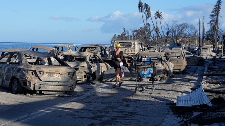 A woman walks through wildfire wreckage in Lahaina, Hawaii on Friday. Hawaii emergency management records show no indication that warning sirens sounded before people ran for their lives from wildfires on Maui that killed multiple people and wiped out a historic town. Instead, officials sent alerts to mobile phones, televisions and radio stations but widespread power and cellular outages may have limited their reach.