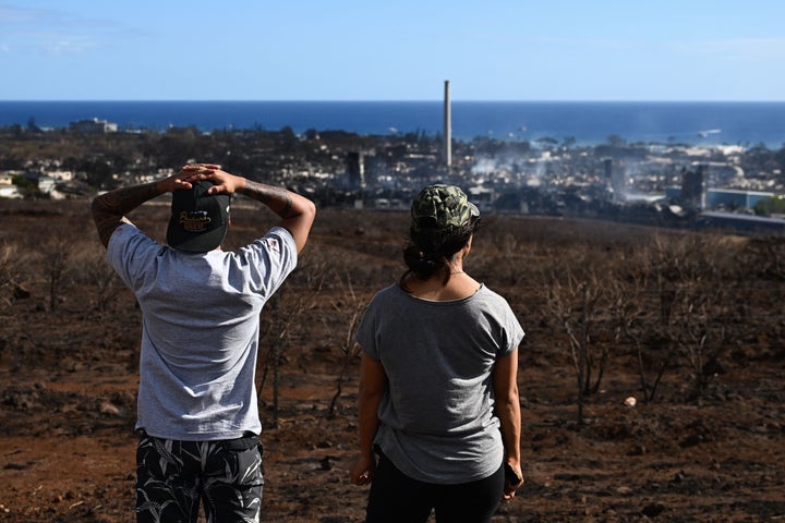 Maui residents John Rey Serrano and Lexie Lara look from a road above Lahaina Town in the aftermath of a wildfire in Lahaina, western Maui, Hawaii on August 11, 2023. A wildfire that left Lahaina in charred ruins has killed at least 67 people, authorities said on August 11, making it one of the deadliest disasters in the US state's history. Brushfires on Maui, fueled by high winds from Hurricane Dora passing to the south of Hawaii, broke out August 8 and rapidly engulfed Lahaina. (Photo by Patrick T. Fallon / AFP) (Photo by PATRICK T. FALLON/AFP via Getty Images)