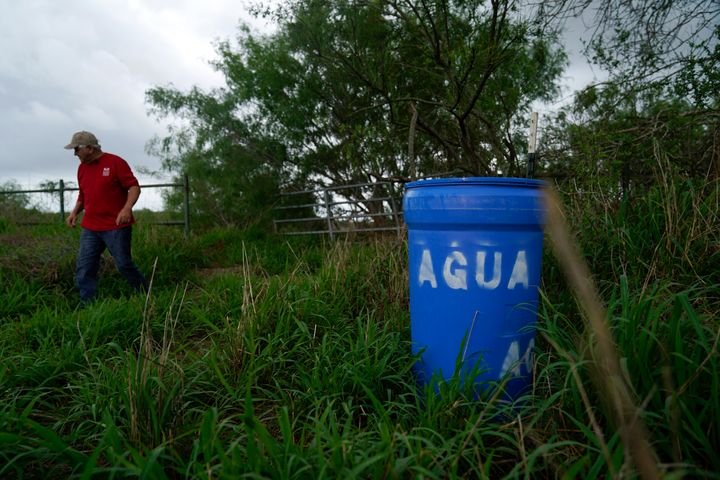 Migrant rights activist Eduardo Canales walks behind one of his blue water drops Saturday, May 15, 2021, in Falfurrias, Texas. Every week, Canales fills up blue water drums that are spread throughout a vast valley of Texas ranchlands and brush. They are there for migrants who venture into the rough terrain to avoid being caught and sent back to Mexico. (AP Photo/Gregory Bull)