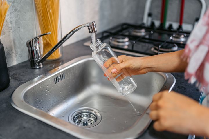 Close-up of a young woman filling a bottle of water over the sink.