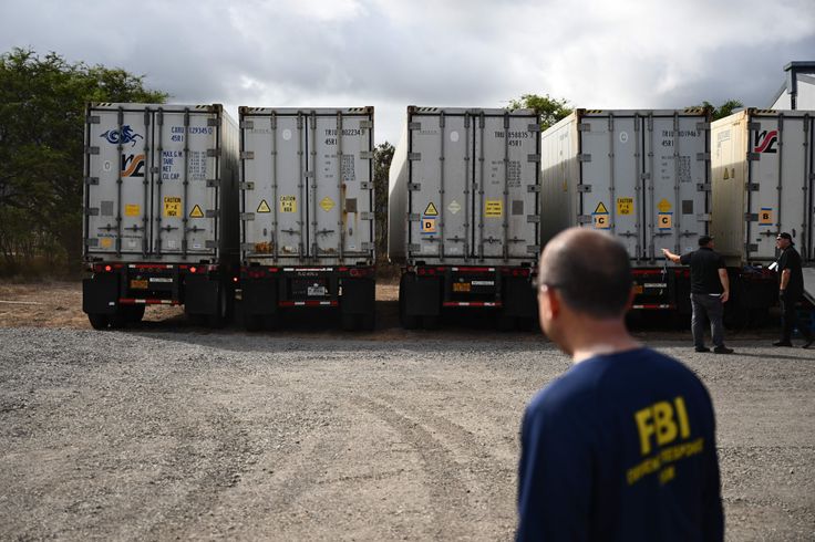 An FBI agent watches on Aug. 14 as two additional refrigerated storage containers arrive adjacent to the Maui Police Forensic Facility in Wailuku, Hawaii, where human remains are stored in the aftermath of the Maui wildfires.