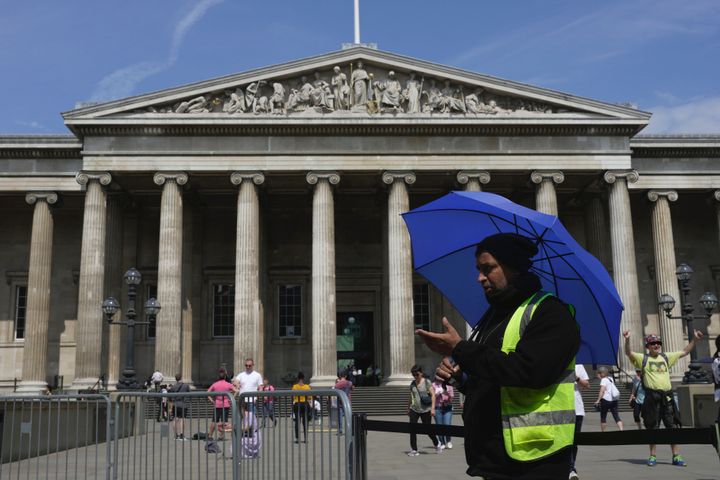 A worker holding an umbrella guides the tourists at British Museum during a hot weather day in Central London, Monday, June 12, 2023.