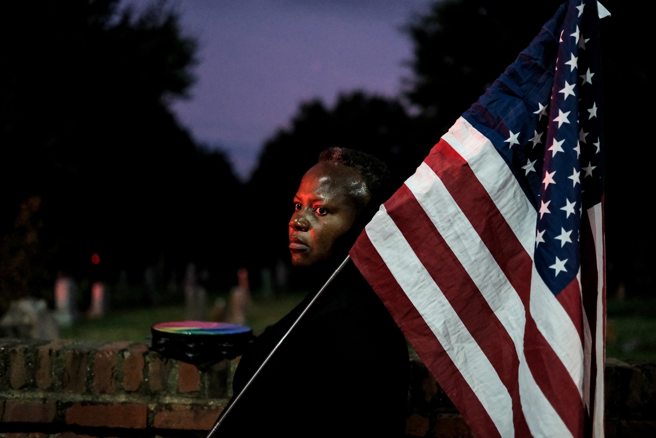 A J6 supporter holds an American flag outside the D.C. jail, with Congressional Cemetery, which is adjacent to the jail, in the background.