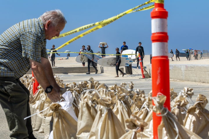 Seal Beach, CA - August 18: John Straub, left, a volunteer with West Orange County Community Emergency Response Team (CERT) loads dozens of sandbags for local residents to fortify their homes as surfers with the M&M Surf School head in ahead of anticipated high surf, strong winds and flooding from the approaching Hurricane Hilary in Seal Beach Friday, Aug. 18, 2023. As Hurricane Hilary continues its march toward Southern California, officials have issued an unprecedented tropical storm watch for the region. The watch is in effect for much of southwestern California, from the San Diego deserts to the San Bernardino County mountains and onto Catalina Island, something the National Hurricane Center said is a first for this area. A tropical storm watch indicates that tropical storm conditions are possible meaning more than 39 mph sustained winds within 48 hours, according to the hurricane center. (Allen J. Schaben / Los Angeles Times via Getty Images)