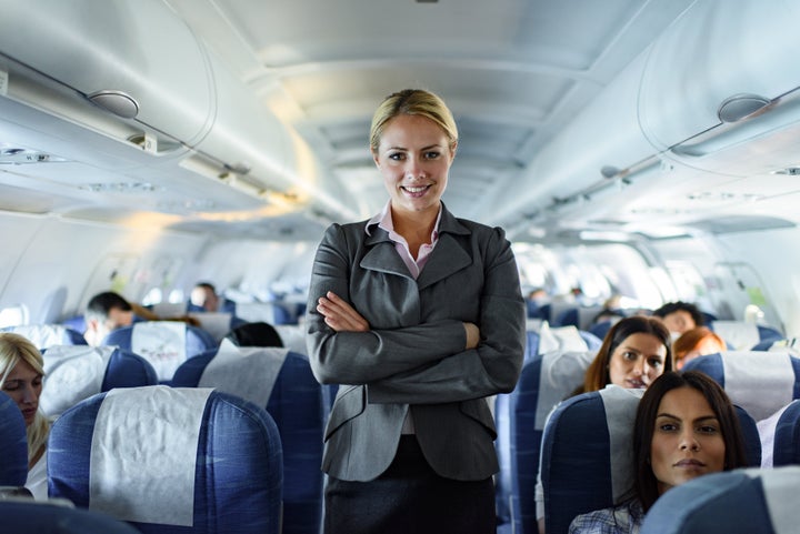 Happy stewardess standing in an airplane with crossed arms and looking at camera.