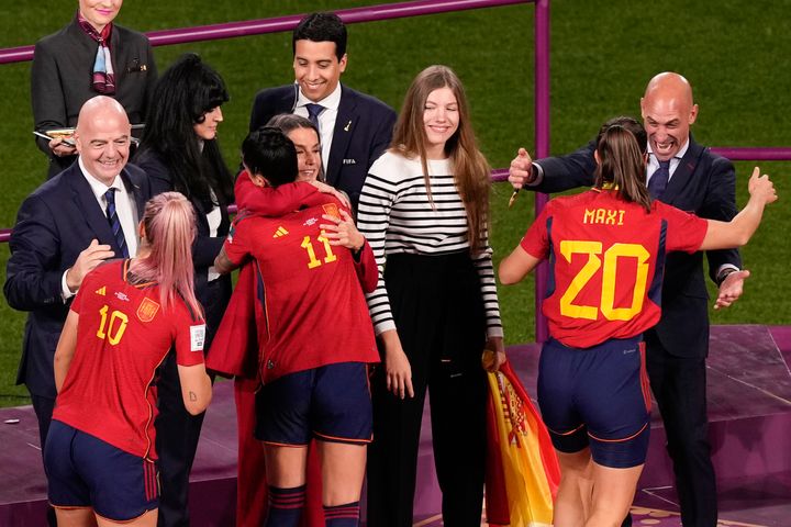Ο πρόεδρος της ισπανικής ομοσπονδίας ποδοσφαίρου, Λουίς Ρουμπιάλες, δεξιά, αγκαλιάζει την Ρότσιο Γκαλβέζ στο βάθρο μετά τη νίκη της Ισπανίας στον τελικό του Παγκοσμίου Κυπέλλου ποδοσφαίρου γυναικών εναντίον της Αγγλίας στο Σίδνεϊ της Αυστραλίας, Κυριακή, 20 Αυγούστου 2023. Φωτογραφία από αριστερά, είναι ο πρόεδρος της FIFA Τζιάνι Ινφαντίνο με την Ισπανίδα Τζένιφερ Ερμόζο, η Ισπανίδα Αλεξία Πουτέλα αγκαλιάζεται από τη βασίλισσα Λετίσια της Ισπανίας καθώς παρακολουθεί η πριγκίπισσα Ινφάντα Σοφία. (AP Photo/Mark Baker)