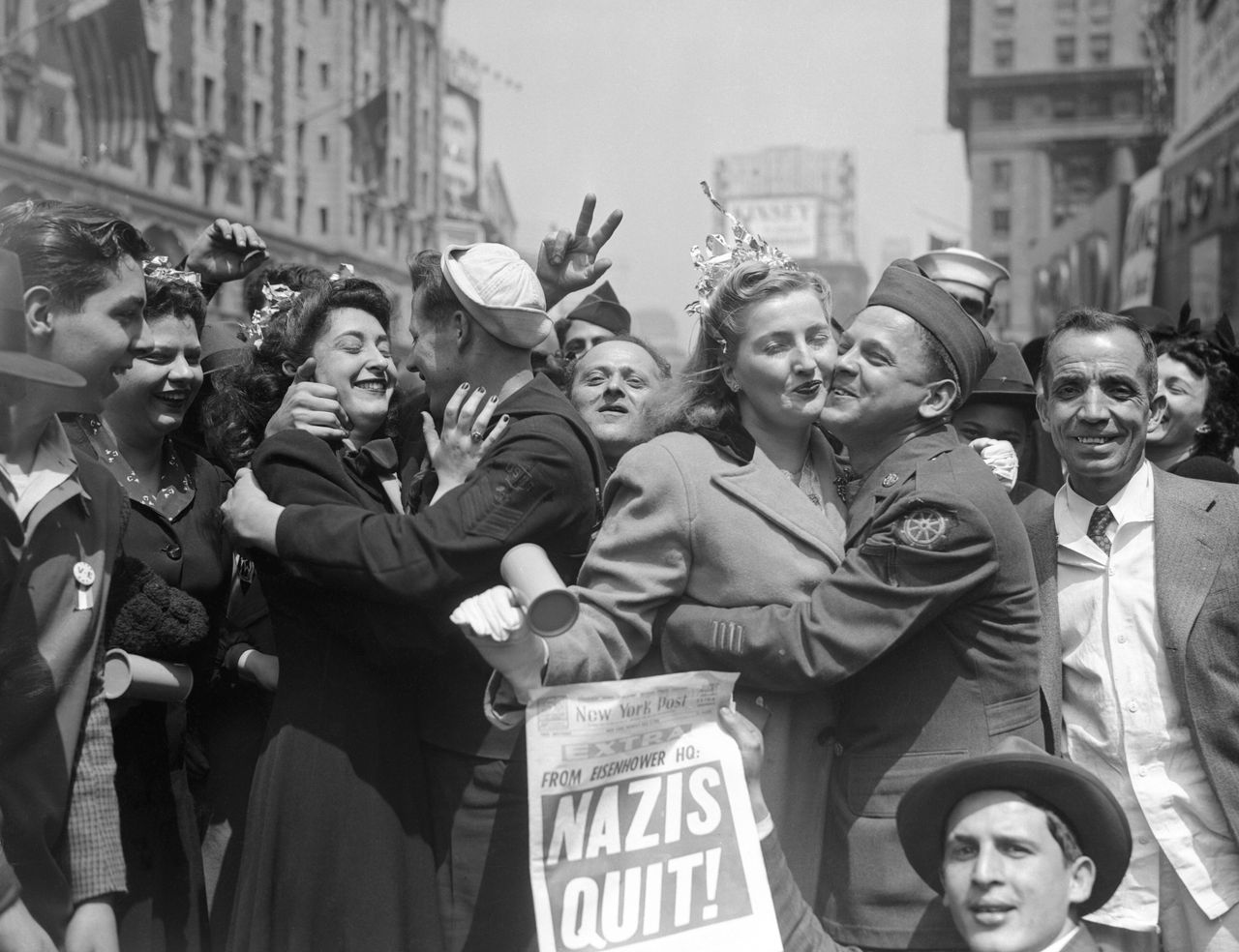 People celebrate on World War II Victory Day with a newspaper headline reading, "Nazis Quit!"