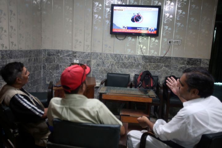 Members of media watch a news channel covering the eight people trapped in a cable car on August 22 at an office in Peshawar, Pakistan.