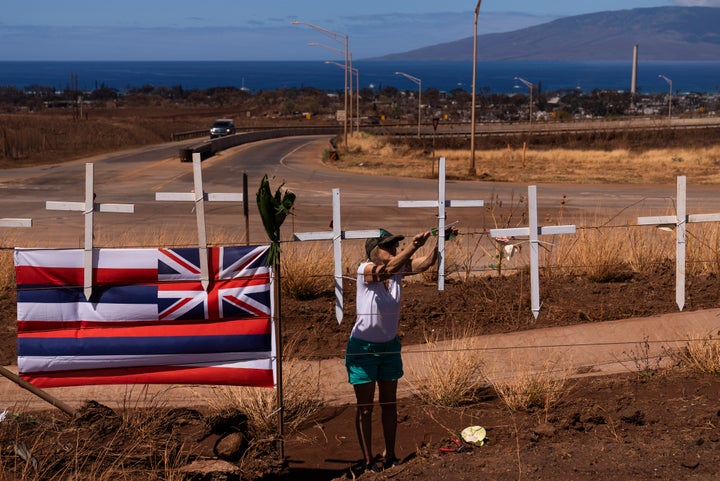 Sunya Schlea ties up roses to crosses along the Lahaina Bypass in Lahaina, Hawaii, Tuesday, Aug. 22, 2023, to honor the victims killed in a wildfire. Two weeks after the deadliest U.S. wildfire in more than a century swept through the Maui community of Lahaina, authorities say anywhere between 500 and 1,000 people remain unaccounted for — a staggering number for officials facing huge challenges to determine how many of those perished and how many may have made it to safety but haven't checked in. (AP Photo/Jae C. Hong)